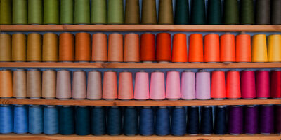 Large spools of a variety of colours resting on a shelf organised in colour order